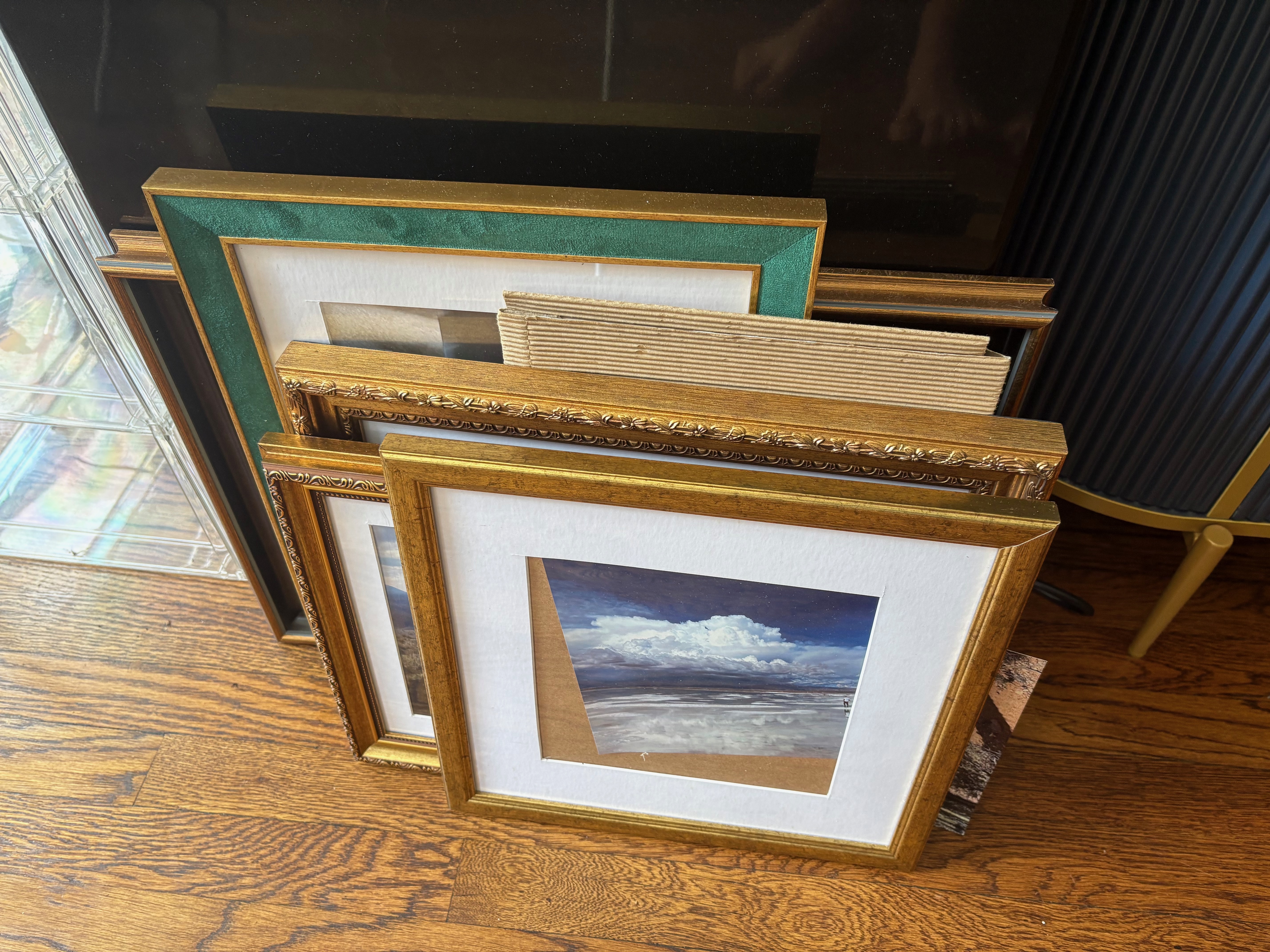 Framed pictures in a variety of frames, stacked and leaning against a freezer
