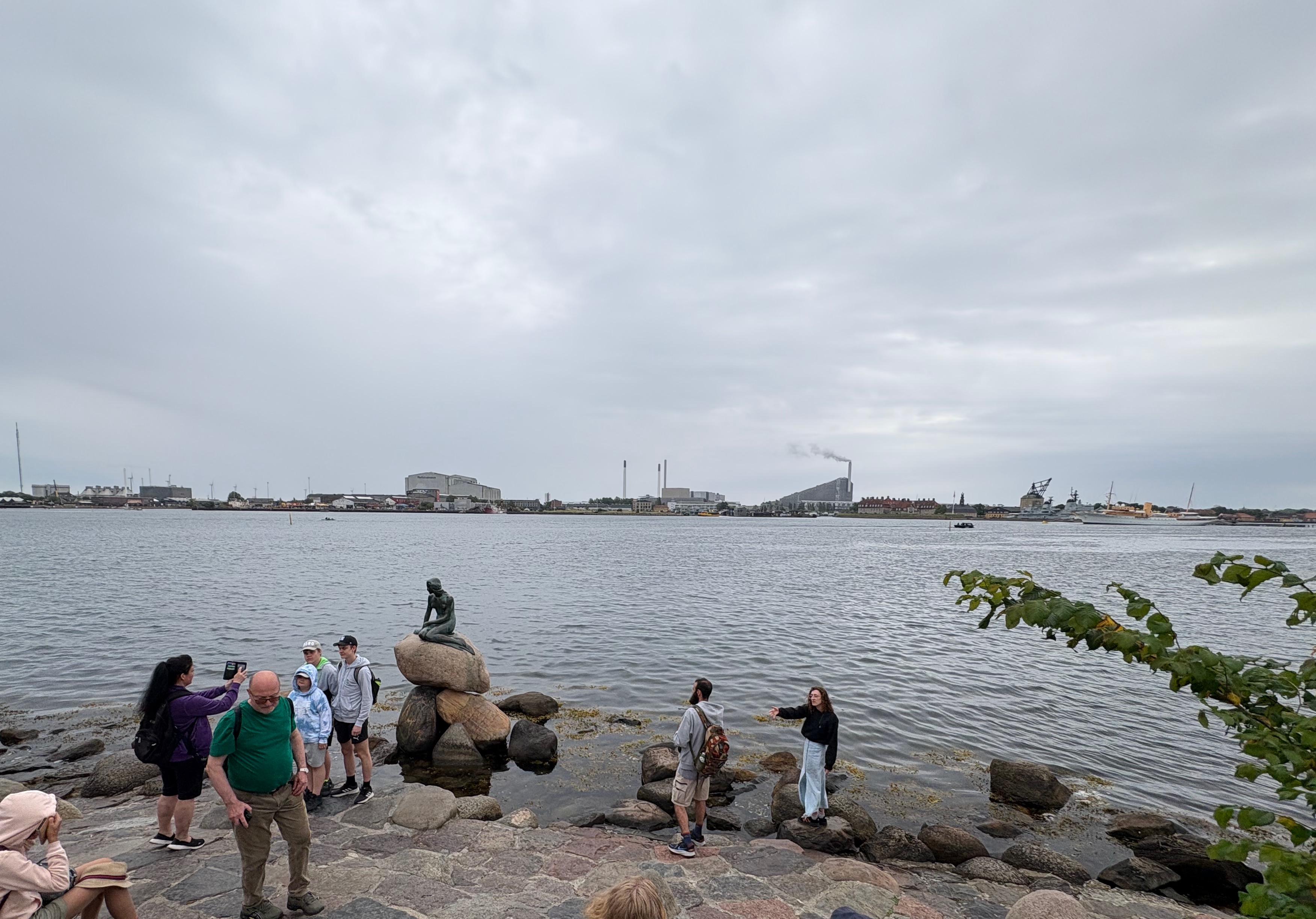 Little Mermaid statue, tourists taking pictures by it, factories in the background